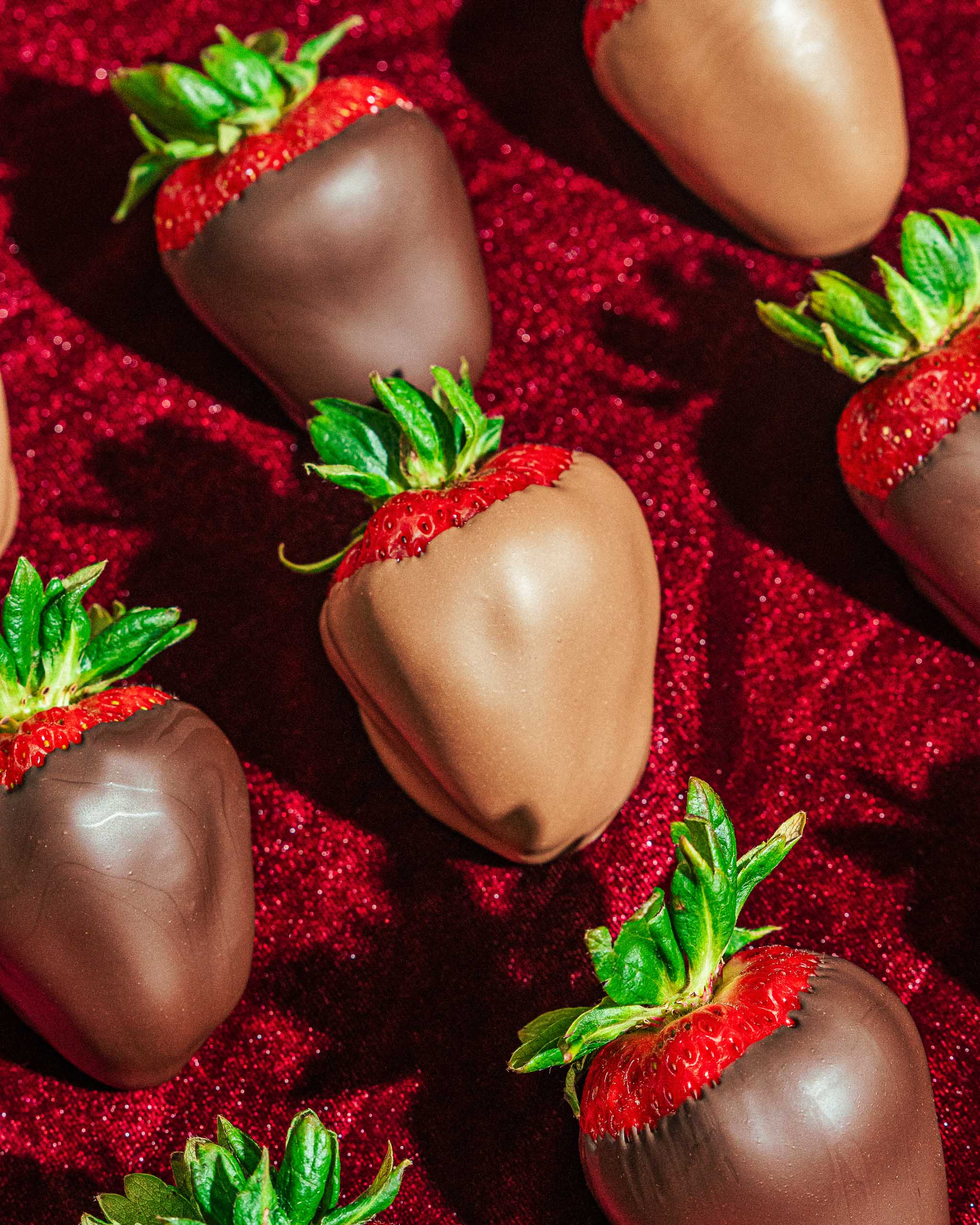 Milk and dark chocolate-covered strawberries on red fabric
